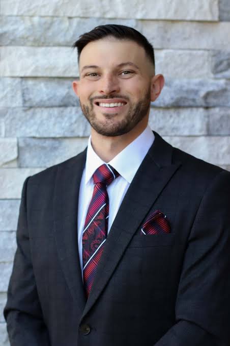 Christopher Kortright in a suit smiling in front of a stone wall
